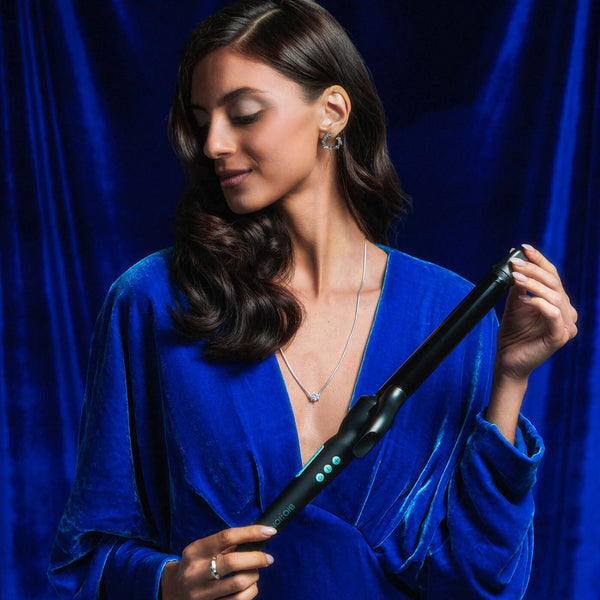 Model with curled hair holding the Long Barrel Curling Iron on a blue background